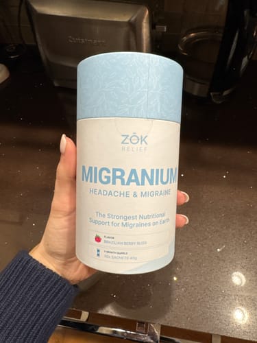 Customer holding a white and blue cylindrical container of ZOK Relief Migranium supplement.