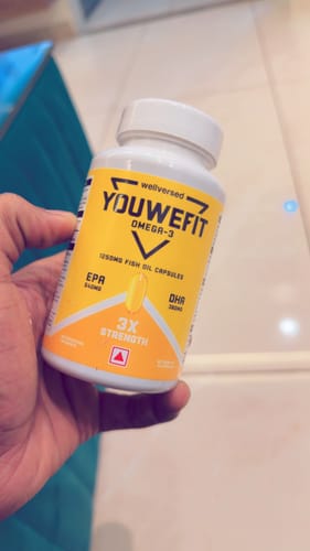 Customer holding a white bottle of YouWeFit Omega-3 Fish Oil capsules with a bright yellow label.