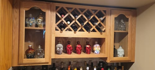 Customer's large collection of colorful Crystal Head Vodka bottles displayed in a wooden bar cabinet.