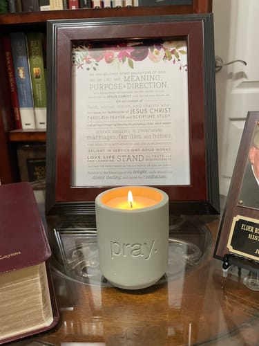 Customer's lit Prayer Candle in a stone vessel on a desk next to a bible and framed art.