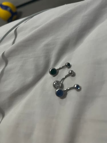 Customer's three Classique Gem Belly Bars with green, clear, and blue gems laid out on a white surface.