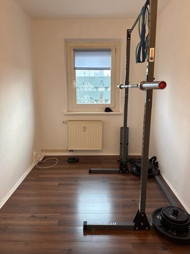 Customer's Original 2029 Power Bar resting on a squat rack in a compact home gym space.