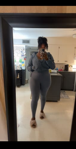 Reviewer in a mirror selfie showing the fit of the Dusty Blue Seamless Ribbed Jumpsuit, worn under a matching zip-up hoodie.