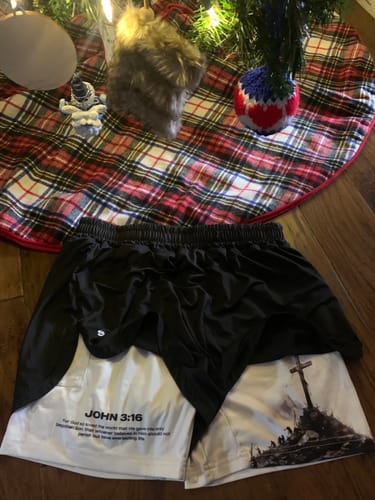 Customer's black and white performance shorts laid flat, showing the John 3:16 scripture and cross graphic.