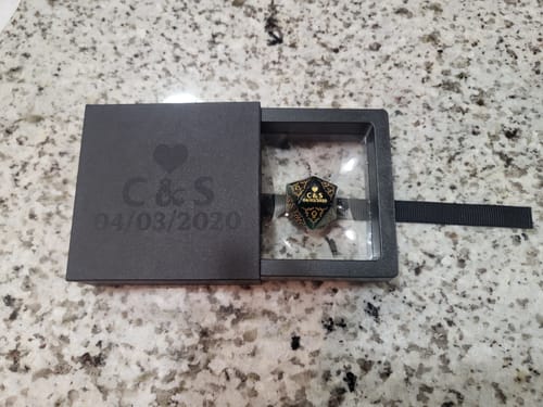 Customer's custom box with engraved initials and date, opened to show a gaming die inside.