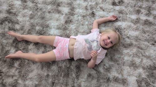 Customer's toddler smiling while lying on the plush, faux fur Mellow Mat.