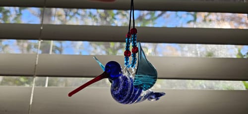 Reviewer's blue Dichroic Twist Glass Hummingbird hanging in a window.