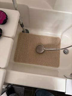 Reviewer's tan In-Shower AquaMat placed in a white shower stall next to a shower seat.