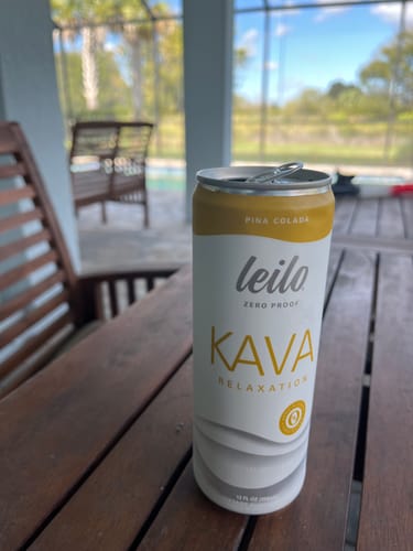 Customer's open can of Pina Colada Kava Tonic on a wooden table by a pool.