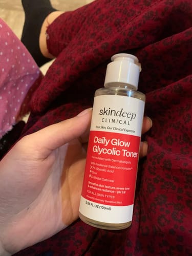 Reviewer holding the Daily Glow Glycolic Toner, showing the full red and white label.