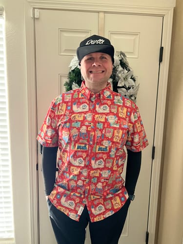 Reviewer smiling while wearing the red Rudolph 'Christmas ‘64' shirt layered over a black long-sleeved shirt indoors.