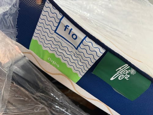 Close-up: Customer's Flo Mattress Ortho showing the brand and 'Aloe Vera' tags on its blue side.