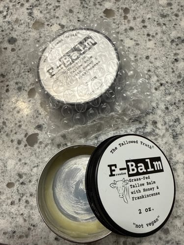 Customer shows a nearly used tin of F-Balm next to a new, bubble-wrapped one on a counter.