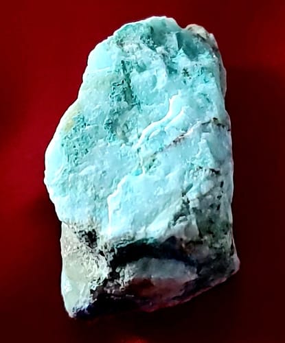 Reviewer's unpolished, light-blue Chrysocolla crystal showing dark inclusions at its base.