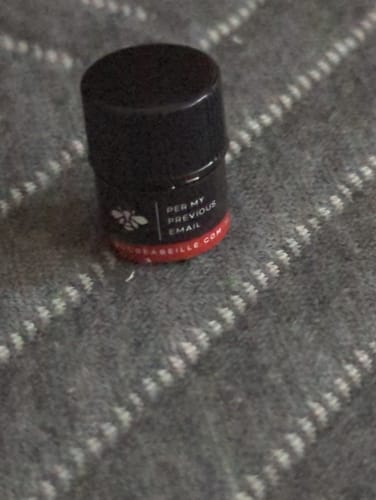 Close-up of a customer's small pot of Per My Previous Email fragrance on a grey textured surface.