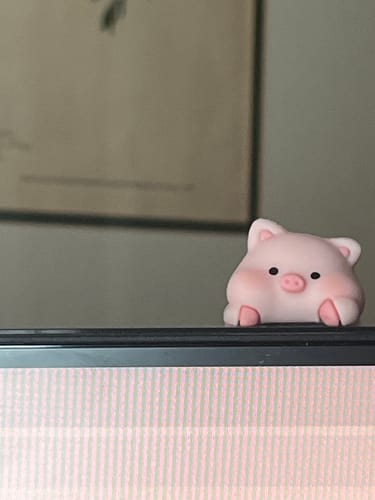 Customer's pink piglet Cuddle Cling Critter peeking over the top of a computer monitor.