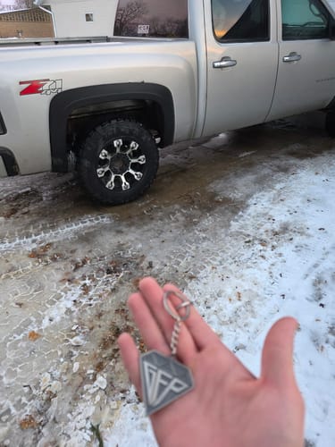 Customer holding the silver DIAMOND KEYCHAIN in their palm, with a truck in a snowy background.