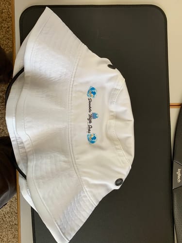 Customer's white custom bucket hat with a blue logo, shown lying flat on a dark surface.