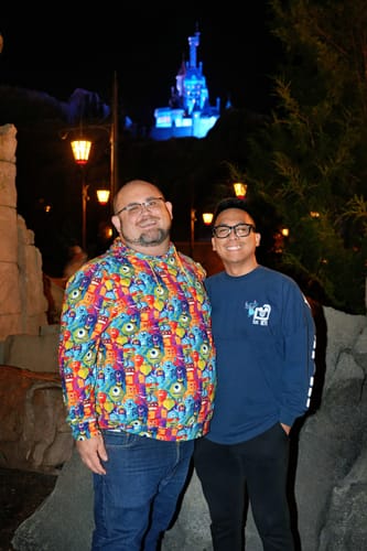 Reviewer smiling while wearing the colorful "The Scare Floor" hoodie with a friend at a theme park at night.
