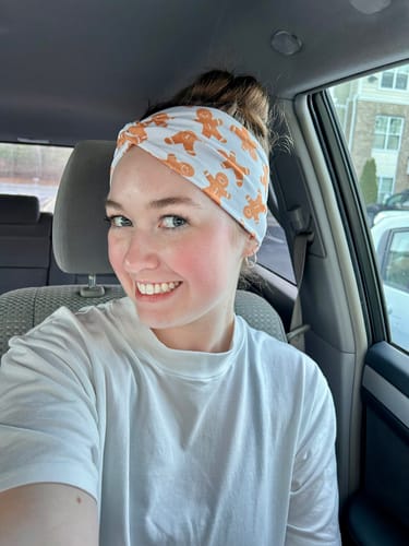 Reviewer smiling in a car, wearing the adorable Gingerbread Cookies Twistband with her hair in a bun.