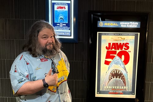 Reviewer gives a thumbs-up while wearing the Jaws "Mapped Out Mayhem" short sleeve shirt at a movie theater.