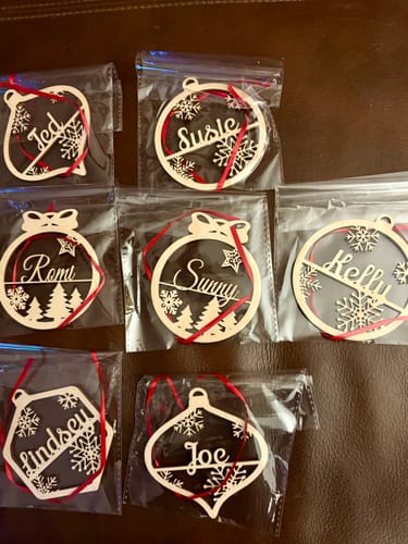Reviewer's collection of personalized wooden Christmas ornaments, each with a name, shown in individual clear packaging.