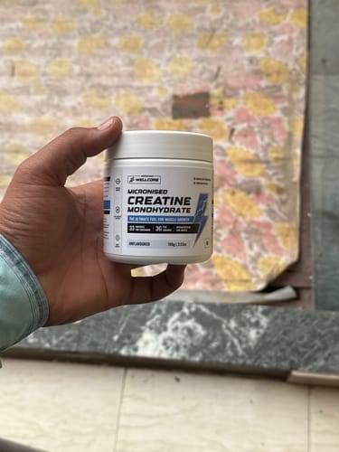 Reviewer's hand holding a white tub of Wellcore Micronised Creatine Monohydrate.