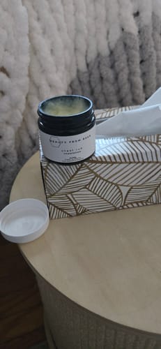 Reviewer's open jar of Chest Rub sitting on a box of tissues on a wooden side table.