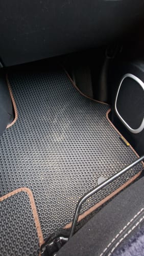 Recenzent pokazuje jednoczęściowy, czarny dywanik samochodowy z brązowym obszyciem w swoim vanie.