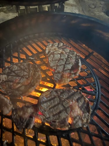 Cliente asando varios cortes de Rib Eye Pieza Básica en una parrilla redonda.