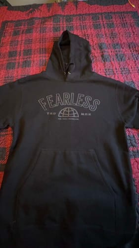 Customer's black FEARLESS HOODIE with a front graphic, laid flat on a red and black plaid surface.
