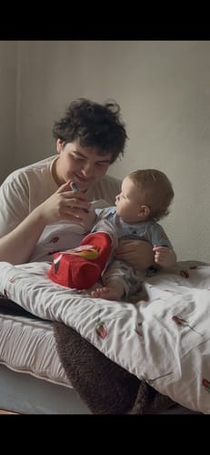 Ein Rezensent sitzt mit einem Baby auf einem Bett und hält das Produkt Hunter Cat Eye.