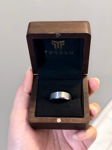 A customer holds open a dark wooden box, showcasing the elegant Sterling ring nestled inside.