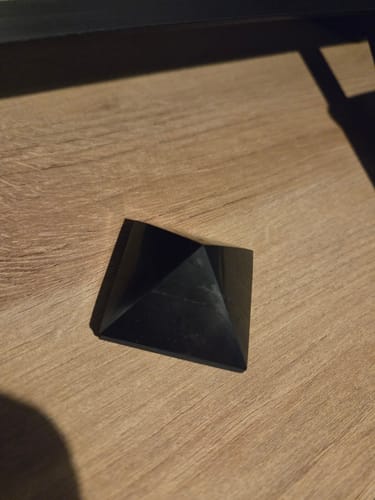 Un client montre sa Pyramide Shungite noire et polie posée sur une surface en bois.