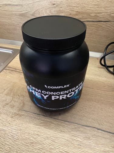 Customer's black tub of Complex CFM Whey Protein sitting on a wooden kitchen counter.