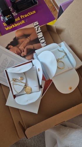 Customer's gold Wave Ring displayed in its open white pouch alongside other jewelry items.