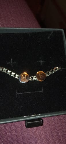 Customer's Vigor bracelet with two charms engraved with 'M' and 'K', shown inside a black jewelry box.