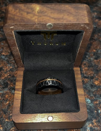 Customer's Stormlight ring with a faceted exterior and rose gold inlay, seen inside its wooden presentation box.