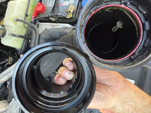 Close-up of a customer comparing the new SPE Cold Side Pipe adapter to the factory part in an engine bay.