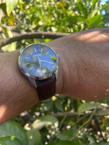 Cliente mostrando su reloj Seiko SNE529 en la muñeca al aire libre, con la esfera oscura y correa de cuero marrón.
