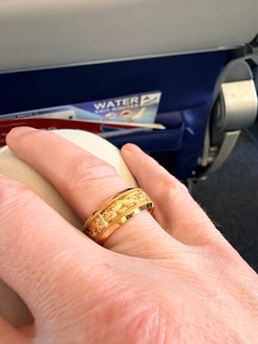 A customer's hand wearing the gold Aureum ring with its textured foil inlay while on an airplane.