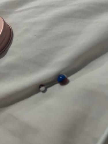 Customer's Pot Luck Acrylic Belly Piercing shown in a close-up, with a blue and red ball on a white surface.