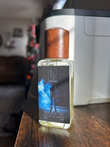 Customer's glass bottle of Woman of Tom perfume with a dark wood cap on a wooden surface.