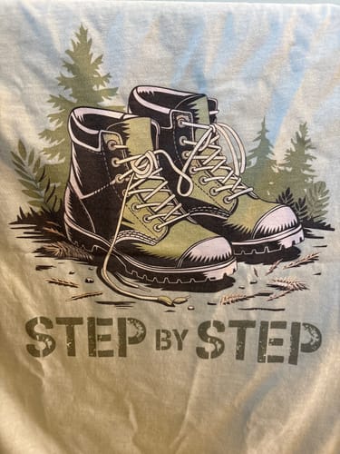 Close-up of a customer's Step By Step T-shirt, showing the detailed graphic of hiking boots and the 'Step by Step' text.
