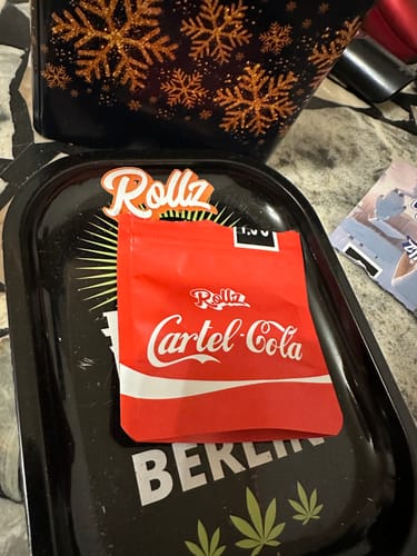 Customer's red pouch of Cartel Cola THCA Flower shown on a black rolling tray.