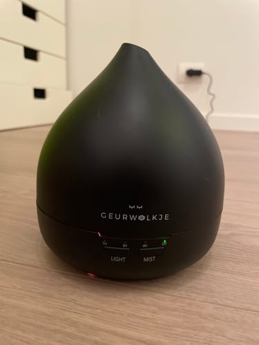 Recensent toont de matzwarte Geurwolkje aroma diffuser, die aan staat op een houten vloer.