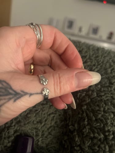 A close-up of a reviewer's thumb wearing the silver-colored Paw Hug Ring with an open, two-paw design.
