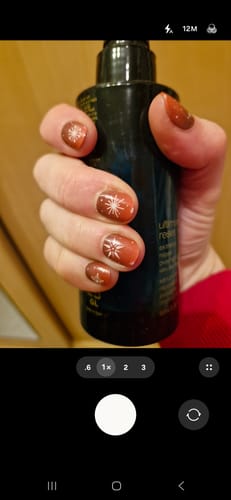 Hand eines Kunden mit Winter Rouge UV-Gel-Nagelfolien, die ein rotes Ombré-Design mit weißen Schneeflocken zeigen.