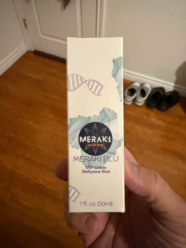 A customer's hand holding the white product box for Meraki Blu Methylene Blue.