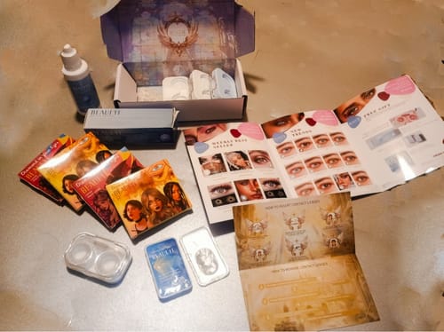 Reviewer's haul of prescription colored contact lenses, including multiple pairs, cases, solution, and pamphlets.